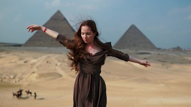 Vertical Instagram video. Young redhead girl in brown dress walking near piramids in Egypt, Cairo - Giza. Copy space