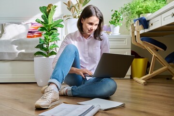 Young female university student studying at home sitting on floor using laptop