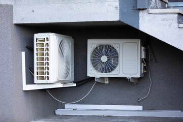 two units of outdoor air conditioners for heat dissipation are hung on the wall outside the building - obrazy, fototapety, plakaty
