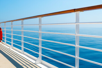 View of the blue ocean and sky from the upper promenade deck of a cruise ship at sea.