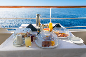 A full room service breakfast on a balcony of a cruise ship cabin at sea including juice, coffee...