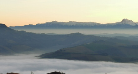 Colline che galleggiano tra nebbia e nuvole mentre il sole tramonta sui monti Appennini