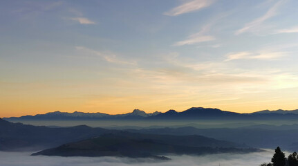 Colline che galleggiano tra nebbia e nuvole mentre il sole tramonta sui monti Appennini