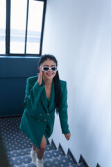 interior of building young latin woman climbing some stairs inside the building wears a jacket and sunglasses , fashion and lifestyle