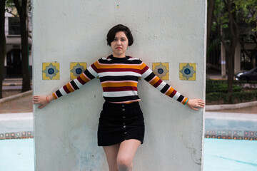 Young woman posing in a white background with tiles in a striped shirt and a black skirt