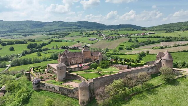 Aerial panning shot of Berze le chatel feudal medieval castle with double enclosure of walls, round towers, donjon, fortified gatehouse on a hill in Central France