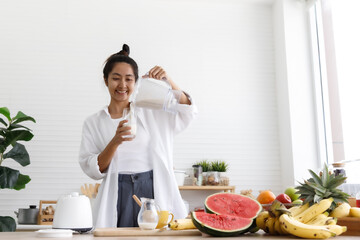 Woman pouring healthy fruit smoothie from Blender juice to glass in the kitchen at home
