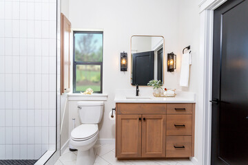 Fototapeta na wymiar A modern farmhouse bathroom with wood cabinets, quartz countertops and black pulls.