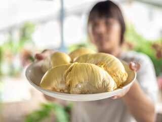 A woman holding a durian shows the yellow durian flesh in a plate.
