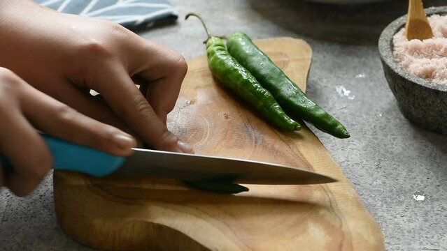 Men's hands cutting green chili pepper on wooden board. 
