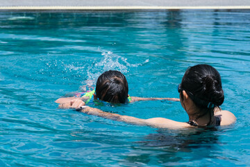 Cute little girl having fun swimming with her mother in the pool on a sunny day. Happy family,...