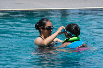 Cute little girl having fun swimming with her mother in the pool on a sunny day. Happy family, mother and her daughter playing in the swimming pool. Summer lifestyle concept.