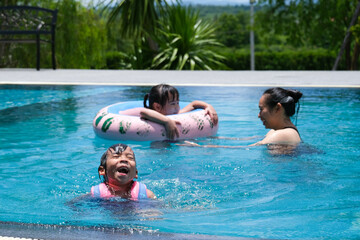 Cute sisters are swimming in life jackets with her mother in the pool on a sunny day. Happy family,...
