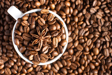 Roasted coffee beans and star anise in a mug on a background of coffee beans.