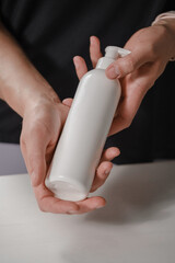 Female hands holding white cosmetic bottle on white background. Skin care, pure beauty, body treatment concept, oil for massage or shampoo with dispenser