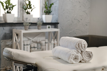 Rolled white towels on massage table in empty salon. Interior of aesthetic clinic, nobody. Modern...