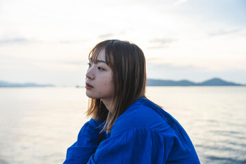 夕暮れの海にいる青いワンピースの女性