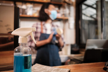 Alcohol sanitizer for healthy protection in a cafe, Asian male barista in face mask use laptop, waiting for coffee order in COVID19 pandemic quarantine, the economic impact for small business startup.