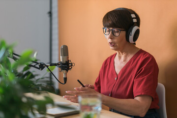 Mature woman making podcast recording for her online show. Attractive business woman using...