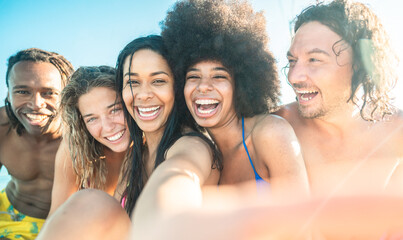 Beautiful brazilian young woman smiling and taking selfie looking at the camera together his friends- Multiracial group of friends relaxing on the beach and having fun together during vacation