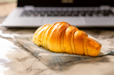 Close-up side view of a brioche croissant, with a laptop out of focus in the background.