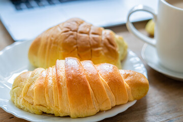 Side view, brioche croissants, on white plate, with cup and laptop out of focus background.