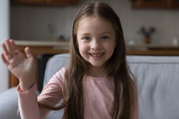 Head shot portrait little girl raise arm makes hello gesture start videocall. Distancing communication to family living abroad, blogging activity, young generation use video call application concept