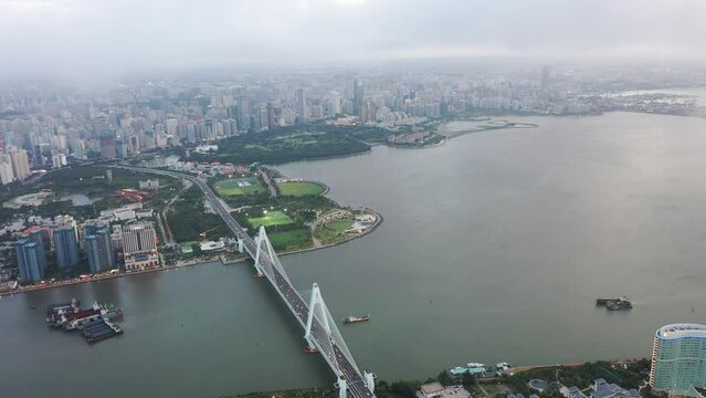Aerial Video of Urban Landscape in the Coastal Central Business District of Haikou City through Clouds, with Landmark Bridge in the View, Hainan Province, China, Asia.