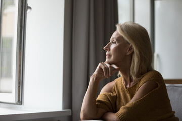 Pensive attractive middle-aged female resting on sofa at home looking out window having nostalgic mood, recollect, deep in thoughts, missing grown up children feeling loneliness. Retirement concept