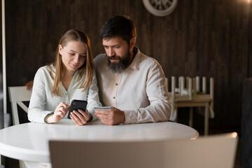 Young couple doing online shopping in cafe using smartphone, bearded man and girl chatting online while sitting in restaurant