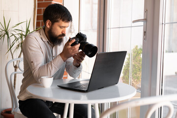 Creative Photographer working with laptop and digital camera at cafe. Professional journalist or freelancer looking at photographs with DSLR camera