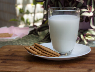 Milk in a glass and biscuits on a white saucer.