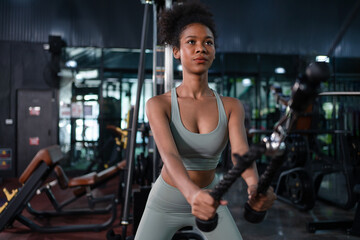 Fototapeta na wymiar Fit young African American female athlete in sportswear exercise bodybuilder pulling down wire cable on gym equipment in fitness center.Workout for good health concept.