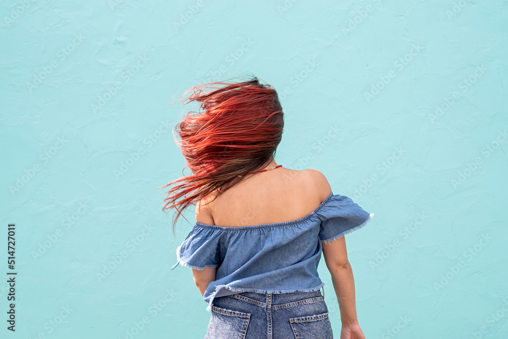 Wall mural cheerful trendy woman with red hair dancing on blue wall background at street