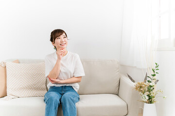 家のソファに座りながら考える日本人女性
