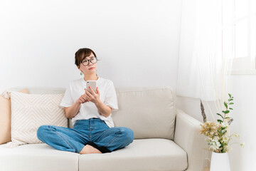 家のソファでスマホを使う女性（考える・困る）
 - obrazy, fototapety, plakaty