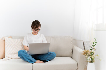 Fototapeta premium 家のソファでパソコンを使うデニム姿の日本人女性（困る・悩む） 