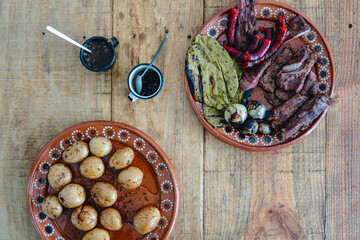 Two plates with meat, nopales, onion, sausages, potatoes and sauces on a wooden table. Mexican dishes. Traditional food. Meat and pork. Barbecue dishes. Above view.