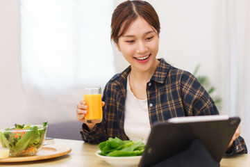 Lifestyle in living room concept, Young Asian woman pointing on tablet and drinking orange juice