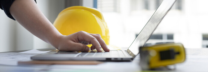 Young man with a laptop plotting a system of building structures in blueprints, Architects or...