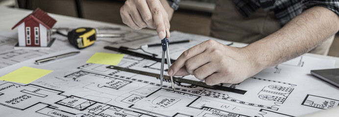 Architectural building design and construction plans with blueprints, Young man was designing a building or architecture with a ruler, pen, pencil, tape measure, architect hat and other equipment.