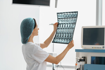 Fototapeta na wymiar Nurse in uniform look on X-ray or MRI scan of the patient spine in operation room
