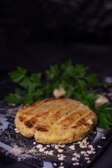 Hamburger medallions made of chickpeas and oats with parsley and a black background.