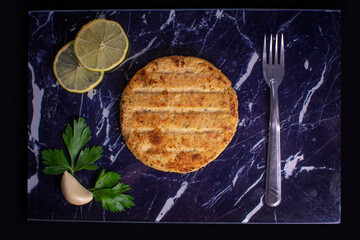 Hamburger medallions made of soya and oats with parsley, garlic, lemon and a black background.