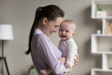 Young mom and cheerful newborn in bodysuit laughing together. Attractive woman hold in arms baby feeling unconditional love, enjoy carefree pleasant time at home. Happy Mothers Day, motherhood concept