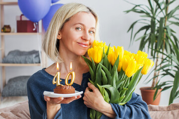 Portrait of happy middle aged woman holding birthday cake with lit candles