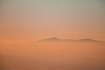 Frosty and foggy morning on the Polish Ochodzita mountain with a view of the Czech Beskydy mountains. Lysa mountain illuminated with orange light. Winter and frosty environment
