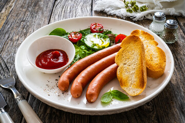 Breakfast - boiled sausages, bread and fresh vegetables served on wooden table
