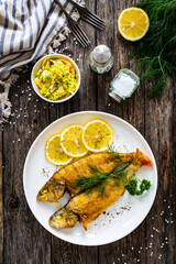 Fried perch with lemon and salad served on wooden table
