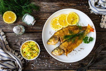 Fried perch with lemon and salad served on wooden table
